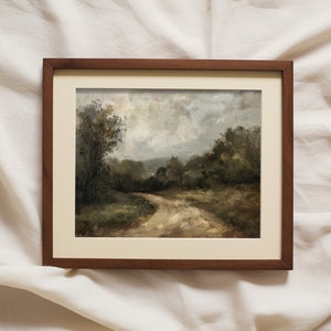 May include: A framed painting of a landscape with a dirt road winding through a forest. The sky is cloudy and the trees are green. The painting is in a brown frame.