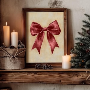 May include: A framed print of a red bow on a beige background. The frame is brown wood and the print is on a shelf with candles and pine branches.