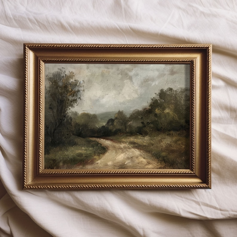 May include: A framed oil painting depicting a landscape scene with a winding dirt road leading through a forest. The painting has a muted color palette with shades of green, brown, and gray.