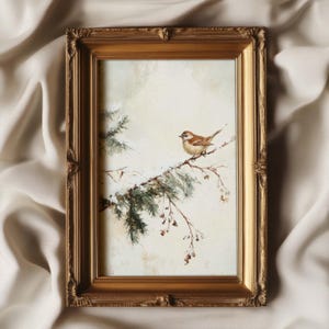K&ouml;nnte beinhalten: Ein gerahmtes Gem&auml;lde eines kleinen braunen Vogels, der auf einem Zweig eines schneebedeckten Nadelbaums sitzt. Das Gem&auml;lde ist vor einem hellen Hintergrund platziert und in einem goldenen Rahmen gefasst.