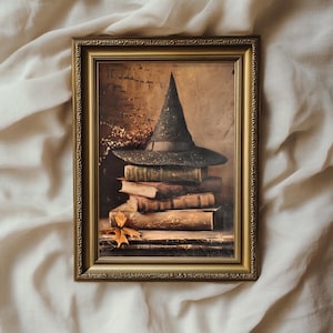 May include: A vintage-style framed print of a witch's hat and a stack of old books. The hat is green and black with a wide brim. The books are brown and have a worn, antique look.