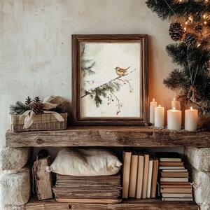 K&ouml;nnte beinhalten: Ein gerahmtes Aquarellbild eines kleinen Vogels, der auf einem schneebedeckten Ast sitzt. Das Bild wird auf einem Holzregal mit Kerzen und B&uuml;chern ausgestellt.