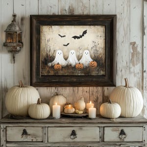 May include: A framed painting of three white ghosts with jack-o'-lantern pumpkins in front of them. The painting is on a whitewashed wood wall with a white lantern and white pumpkins in the foreground.