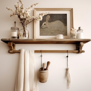 May include: A wooden shelf with a white rabbit illustration in a frame, two clear glass jars, a white ceramic jar, and a white towel hanging from a metal rod.