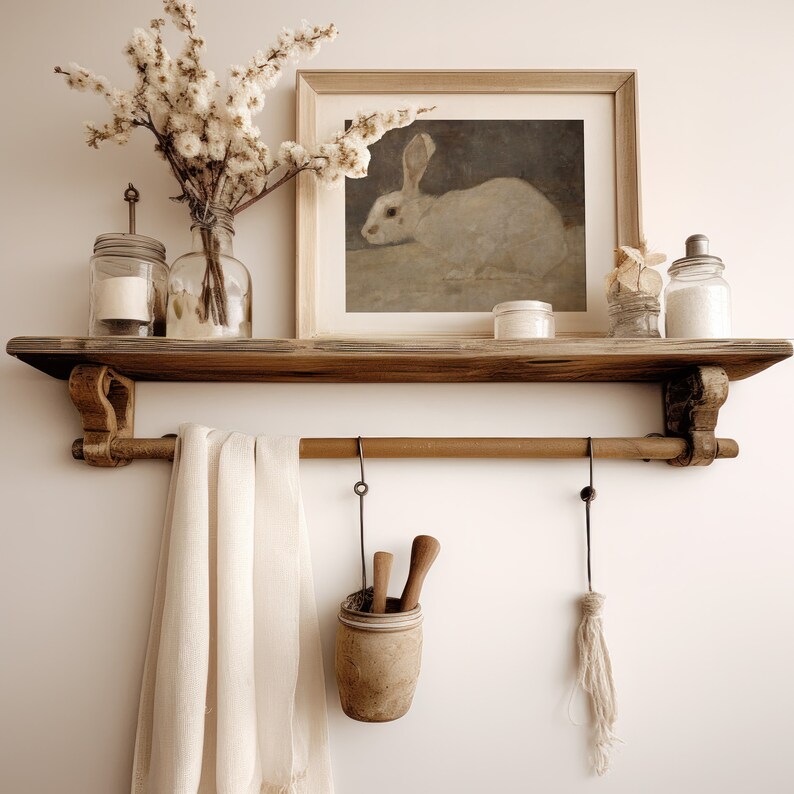 May include: A wooden shelf with a white rabbit illustration in a frame, two clear glass jars, a white ceramic jar, and a white towel hanging from a metal rod.