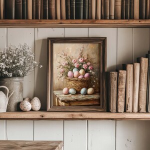 May include: A framed painting of a basket filled with pastel colored Easter eggs, surrounded by pink flowers. The basket is sitting on a wooden table.