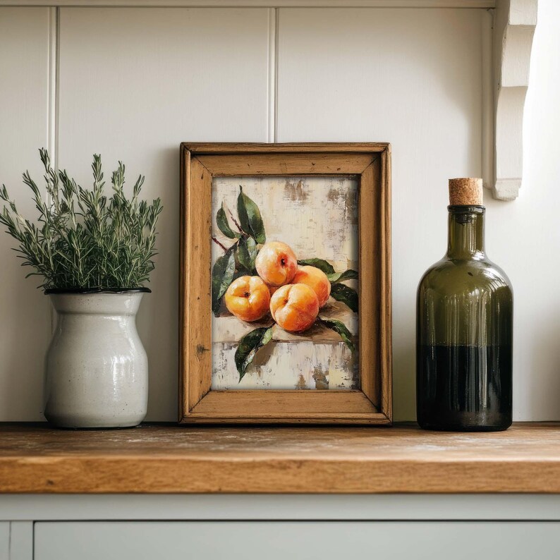 May include: A framed painting of a still life with four ripe peaches on a white background. The peaches are arranged in a cluster, with the largest one in the center. The painting is set against a white wall, with a vase of greenery and a bottle of dark liquid on the shelf below.