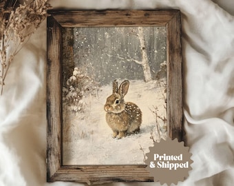 May include: A framed print of a brown rabbit in a snowy forest setting. The rabbit is looking to the left and has its ears perked up. The background is a snowy forest with trees and snow on the ground. The frame is a rustic brown wood frame.