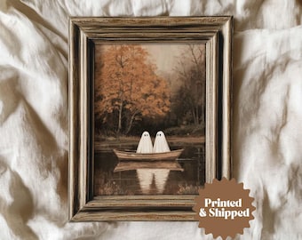 May include: A framed art print depicting two ghost figures in a boat on a lake. The artwork has a vintage aesthetic with a sepia-toned colour palette. The frame is a distressed, light brown colour. The text "Printed & Shipped" is on a brown sticker.