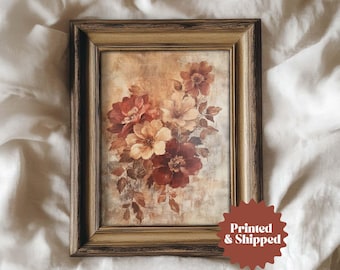 Pode incluir: Uma impressão floral emoldurada com um buquê de flores vermelhas e creme com folhas marrons. A obra de arte está em uma moldura retangular dourada. A imagem tem uma estética vintage.