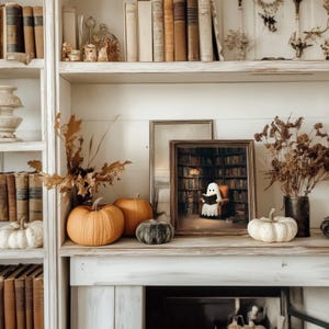 Pode incluir: Uma prateleira decorativa com tema de outono com ab&oacute;boras, folhagens secas e uma obra de arte emoldurada de um fantasma lendo em uma biblioteca. A prateleira &eacute; preenchida com livros antigos e itens decorativos.