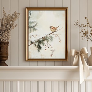 K&ouml;nnte beinhalten: Ein gerahmtes Aquarellbild eines kleinen braunen Vogels, der auf einem schneebedeckten Zweig einer Kiefer sitzt. Der Hintergrund ist in einem sanften, ged&auml;mpften Beige gehalten.