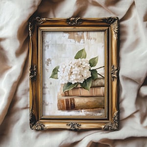 Puede incluir: Una pintura enmarcada de una hortensia blanca descansando sobre una pila de libros antiguos. El fondo es de color beige claro.