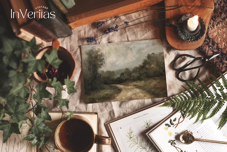 May include: A vintage painting of a winding dirt road through a forest, framed and displayed on a table with books, plants, and a candle. The painting has a rustic, earthy feel.