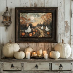 Könnte beinhalten: Ein gerahmtes Halloween-Gemälde zeigt Geister, Kürbisse und einen Waldweg. Weiße Kürbisse, Kerzen und eine dekorative Laterne stehen auf einem alten Holztisch und schaffen eine herbstliche Atmosphäre.