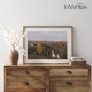 May include: A framed painting of a rural landscape with a small village in the distance. The painting is set against a cloudy sky and features a few trees in the foreground. The painting is displayed on a wooden dresser with a vase of white flowers.