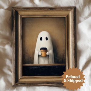 May include: A framed print depicting a white ghost with black eyes, holding a coffee cup. The cup is brown with the word "Coffee" on it. The background is a warm, neutral tone. The frame is a light brown colour, adding a vintage feel to the artwork.
