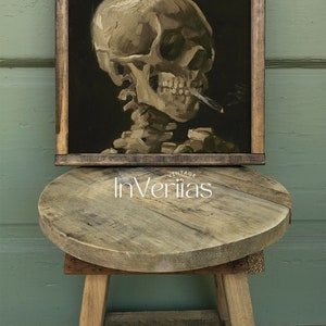 May include: A framed painting of a human skull smoking a cigarette. The skull is painted in a realistic style with a dark background. The painting is framed in a dark wood frame.