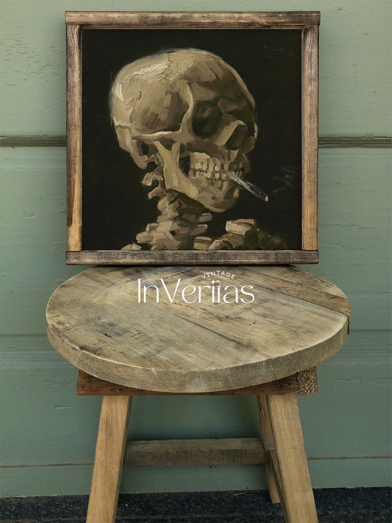 May include: A framed painting of a human skull smoking a cigarette. The skull is painted in a realistic style with a dark background. The painting is framed in a dark wood frame.