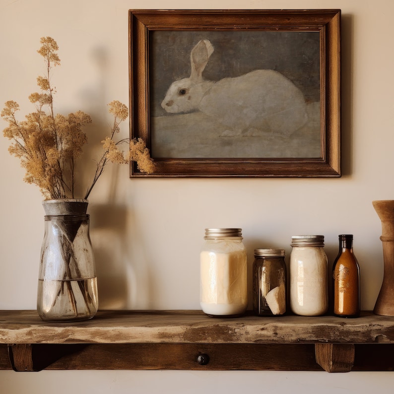 May include: A white rabbit in a framed painting hangs above a wooden shelf with four glass jars and a bottle. The jars have lids and contain a white substance. The bottle is brown and has a label.