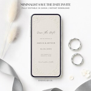 Puede incluir: Un tel&eacute;fono inteligente que muestra una invitaci&oacute;n digital de reserva de fecha con bordes florales y el texto Save the Date, Amelia & Arthur, 06.06.20XX, Love Garden Villa, Pearlsville, Miami. Dos anillos plateados y una cinta gris est&aacute;n cerca.