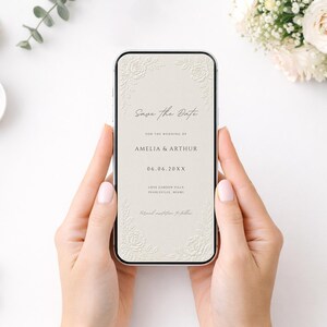 Puede incluir: Un tel&eacute;fono inteligente que muestra una invitaci&oacute;n de boda digital Save the Date sobre un fondo crema con esquinas florales en relieve. El texto dice Save the Date, for the wedding of Amelia & Arthur, 06.06.20XX, Love Garden Villa, Pearlesville, Miami.