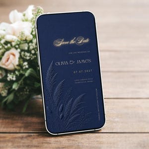 May include: A smartphone displaying a navy blue digital Save the Date wedding invitation. The screen features gold text reading Save the Date, Olivia & James, and 07.07.2027, alongside an embossed-style graphic of pampas grass and wheat stalks.