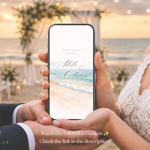 May include: A smartphone displaying a digital wedding invitation with the text WE'RE GETTING MARRIED and the names Adele & Oliver. The screen features a graphic of a sandy beach with turquoise ocean waves under a soft sunset sky.
