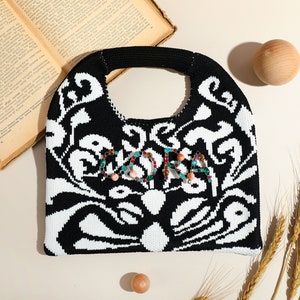 May include: Black and white crocheted tote bag with a beaded design that spells out "LOVE". The bag has a black handle and is decorated with colorful beads.