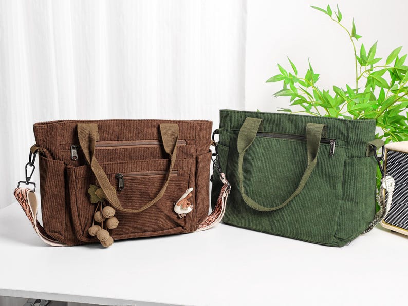 Puede incluir: Dos bolsos tote de pana. Uno es marr&oacute;n con asa marr&oacute;n, un adorno decorativo y una correa estampada. El otro es verde con asa verde. Ambos bolsos tienen m&uacute;ltiples bolsillos y cierre de cremallera.