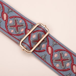 May include: A blue and red patterned strap with a gold metal buckle. The strap has a repeating pattern of stylized flowers and crosses.