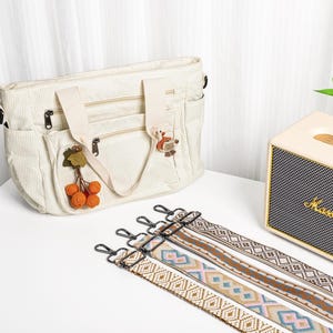 Puede incluir: Bolso tote de pana color crema con m&uacute;ltiples bolsillos y cremalleras, adornado con abalorios decorativos. Incluye varias correas para el hombro estampadas con cierres met&aacute;licos. Un altavoz crema y negro est&aacute; en el fondo.