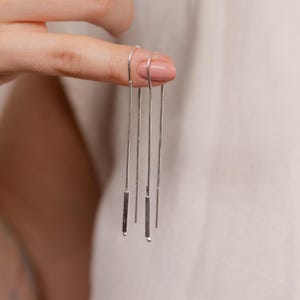 Op de afbeelding: Zilveren oorhangers met een dunne ketting en een klein staafje aan het einde.