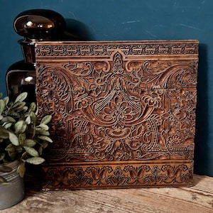 Könnte beinhalten: Ein rechteckiger Holzdruckblock mit tief geschnitzten, komplexen Blumen- und Geometriemustern auf der Oberfläche. Das dunkelbraune Holz zeigt ein symmetrisches Design mit kunstvollen Schnörkeln, Blattmotiven und dekorativen Rändern.