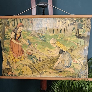 Op de afbeelding: Een wandkleed in vintage-stijl met een gedrukte illustratie van twee figuren in traditionele kleding en een kabouter in een bosrijke omgeving. De scène toont een kabouter met een lange baard die vastzit in een boomstam.