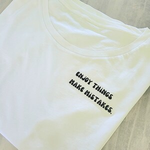 Könnte beinhalten: Weißes T-Shirt mit schwarzem Text, der "Enjoy things make mistakes." lautet.