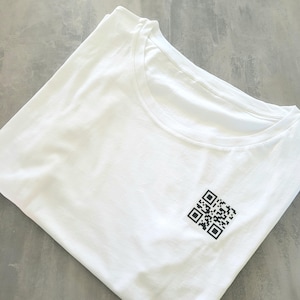 Può includere: Maglietta bianca con un codice QR nero stampato sul davanti.