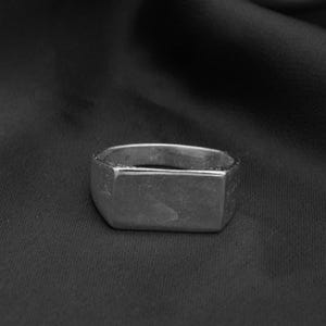 May include: A silver rectangular ring with a smooth, slightly textured surface.