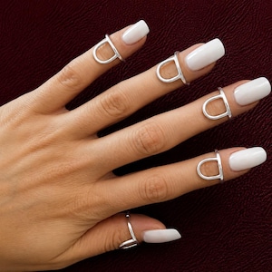 May include: A set of five silver-toned nail rings, each featuring a smooth, U-shaped design that sits securely on the upper portion of the finger, just below the nail bed, providing a sleek and polished look for all five fingers.
