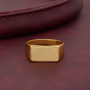 A simple, smooth silver-tone signet ring features a prominent rectangular face suitable for engraving.