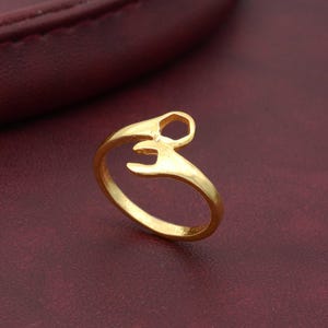 Puede incluir: Un anillo de color dorado con un diseño de llave inglesa. El anillo está hecho de metal y tiene un acabado liso.