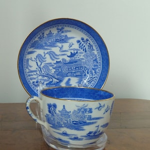 May include: A blue and white porcelain teacup and saucer set with a gold trim. The set features a traditional Chinese landscape design with a pagoda, trees, and birds.