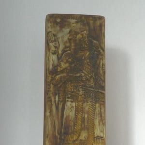 May include: A rectangular ceramic vase with a raised relief design of a figure in a robe. The vase is a light brown colour with a green glaze.