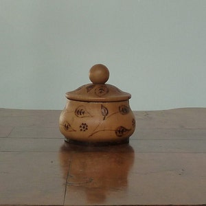 May include: A small wooden box with a lid, decorated with a floral design. The box is brown and has a smooth finish.