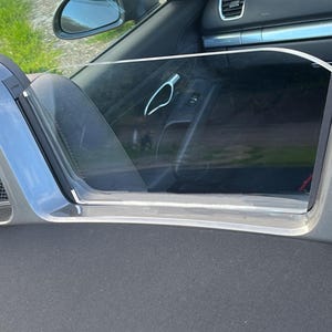 May include: A gray convertible car with a black interior. The car has a clear wind deflector installed on the back window.