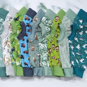 Könnte beinhalten: Eine Sammlung von zehn Baby-Bodys in verschiedenen Grüntönen und Blau mit verschiedenen Tier- und Naturmotiven. Die Bodys haben lange Ärmel und sind aus weichem, bequemem Stoff.