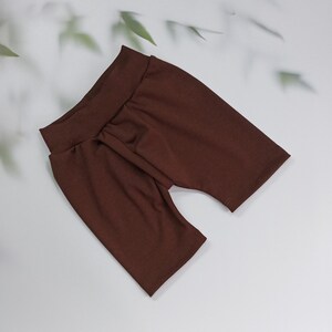 Pu&ograve; includere: Un paio di pantaloncini da ciclista marroni realizzati in un tessuto morbido ed elastico. I pantaloncini hanno una vita alta e un design aderente. Il colore &egrave; un marrone ricco e caldo, esposto su una superficie bianca.