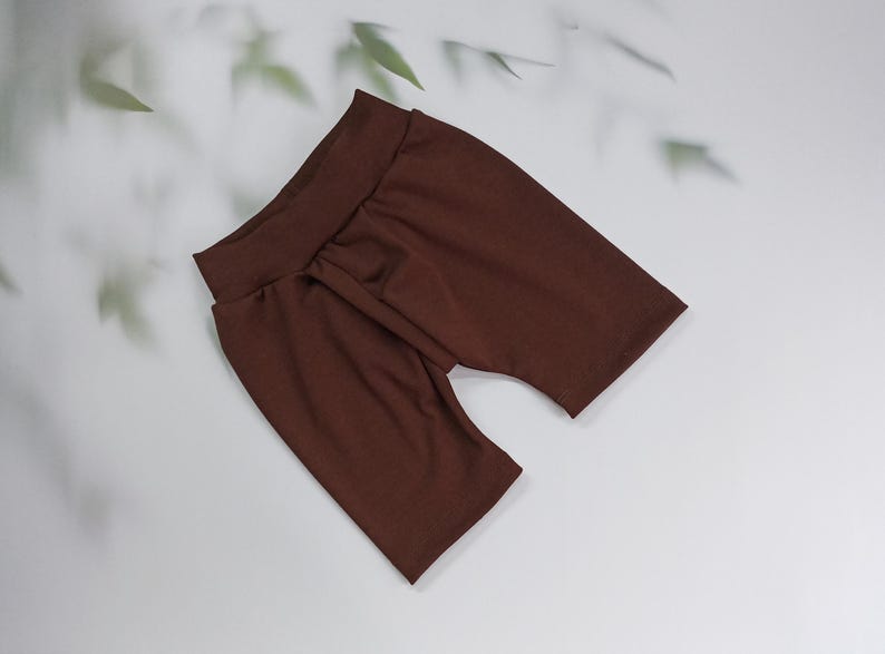Pu&ograve; includere: Un paio di pantaloncini da ciclista marroni realizzati in un tessuto morbido ed elastico. I pantaloncini hanno una vita alta e un design aderente. Il colore &egrave; un marrone ricco e caldo, esposto su una superficie bianca.
