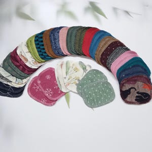 Könnte beinhalten: Eine Sammlung wiederverwendbarer Abschminkpads in verschiedenen Farben und Mustern, darunter Grün, Blau, Rot und Weiß. Die Pads sind in einer Halbkreisform angeordnet, wobei einige übereinander gestapelt sind.