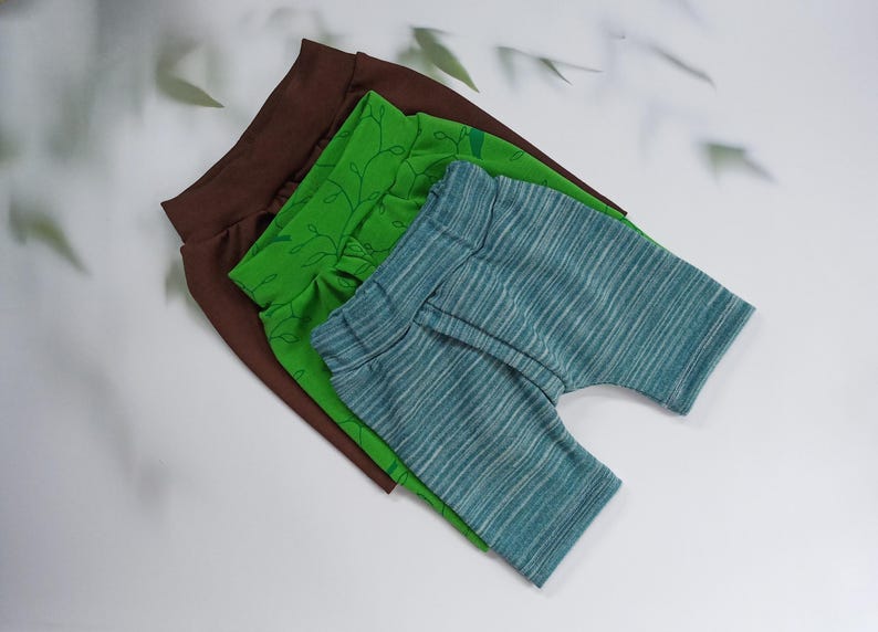 Pu&ograve; includere: Tre paia di pantaloncini per bambini in marrone, verde e blu. Il paio marrone &egrave; tinta unita, il paio verde ha un motivo a foglie e il paio blu ha un motivo a righe. I pantaloncini sono impilati su una superficie bianca.